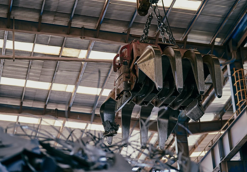 A steel grapple suspended above scrap metal inside an industrial shed