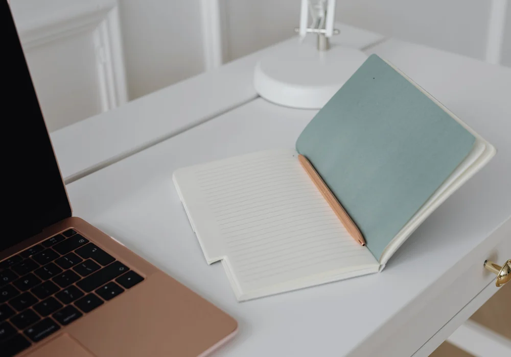 Open lined notebook and pencil beside a laptop with a dark screen on a white desk