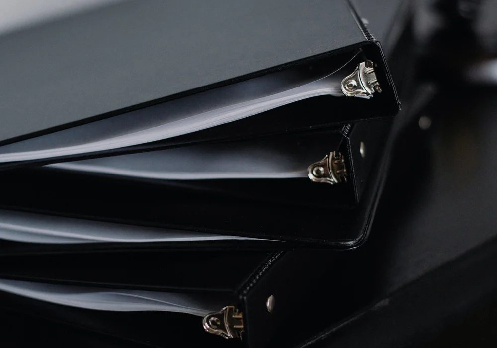 Unlabeled black document binders stacked neatly on a desk