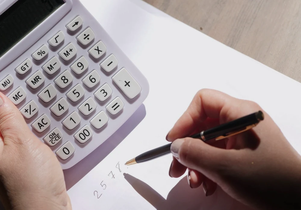 Hands using a calculator and writing simple numbers on a sheet of paper.