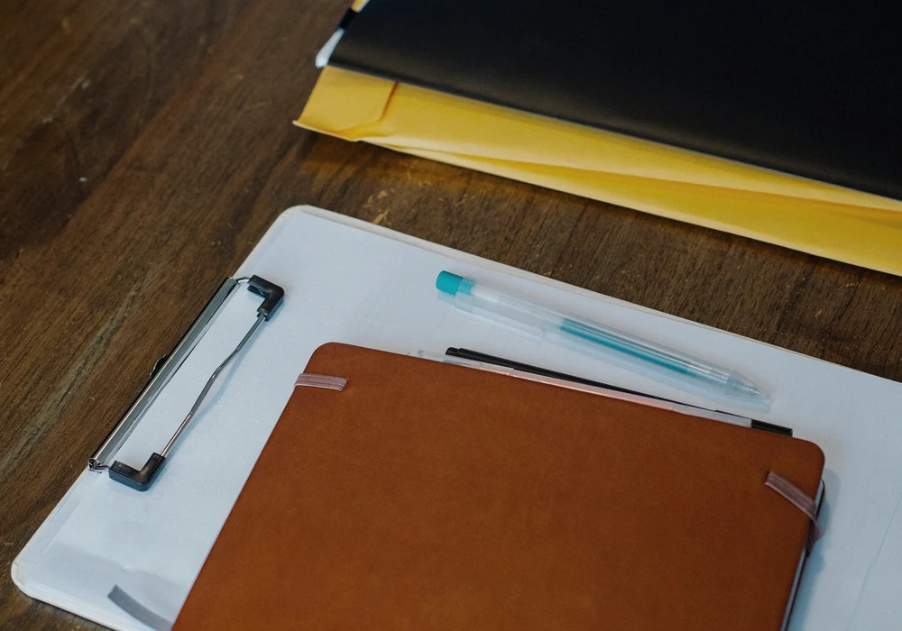 Closed notebook on a clipboard beside neatly stacked folders and pens.