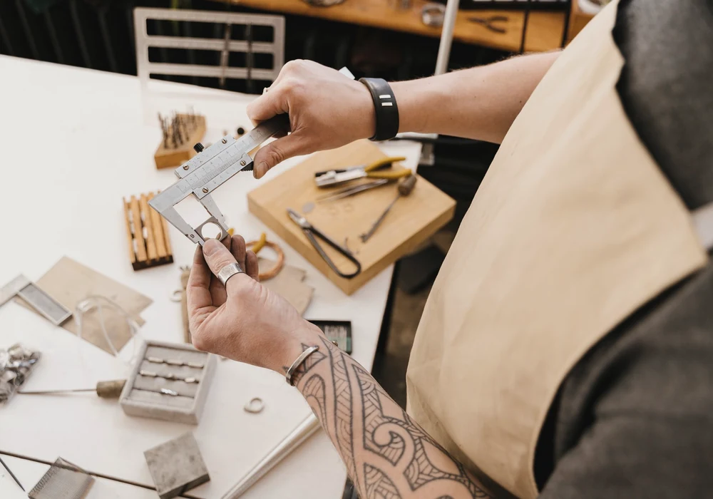 Hands measuring a metal ring with a vernier caliper at a workshop bench.
